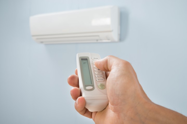 Man Adjusting Temperature Of Air Conditioner Using Remote