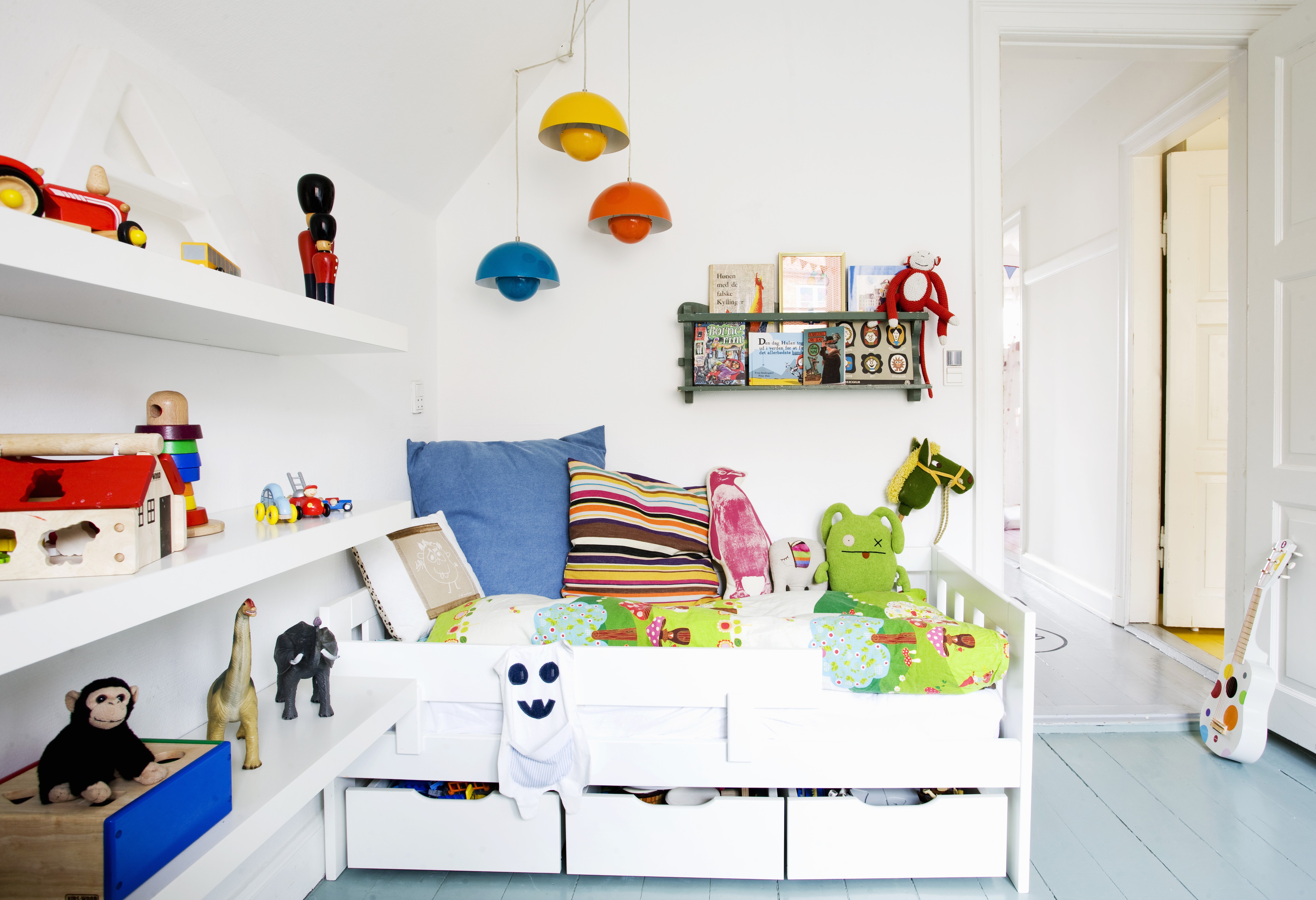 White bed with drawers and shelves of toys in child's bedroom