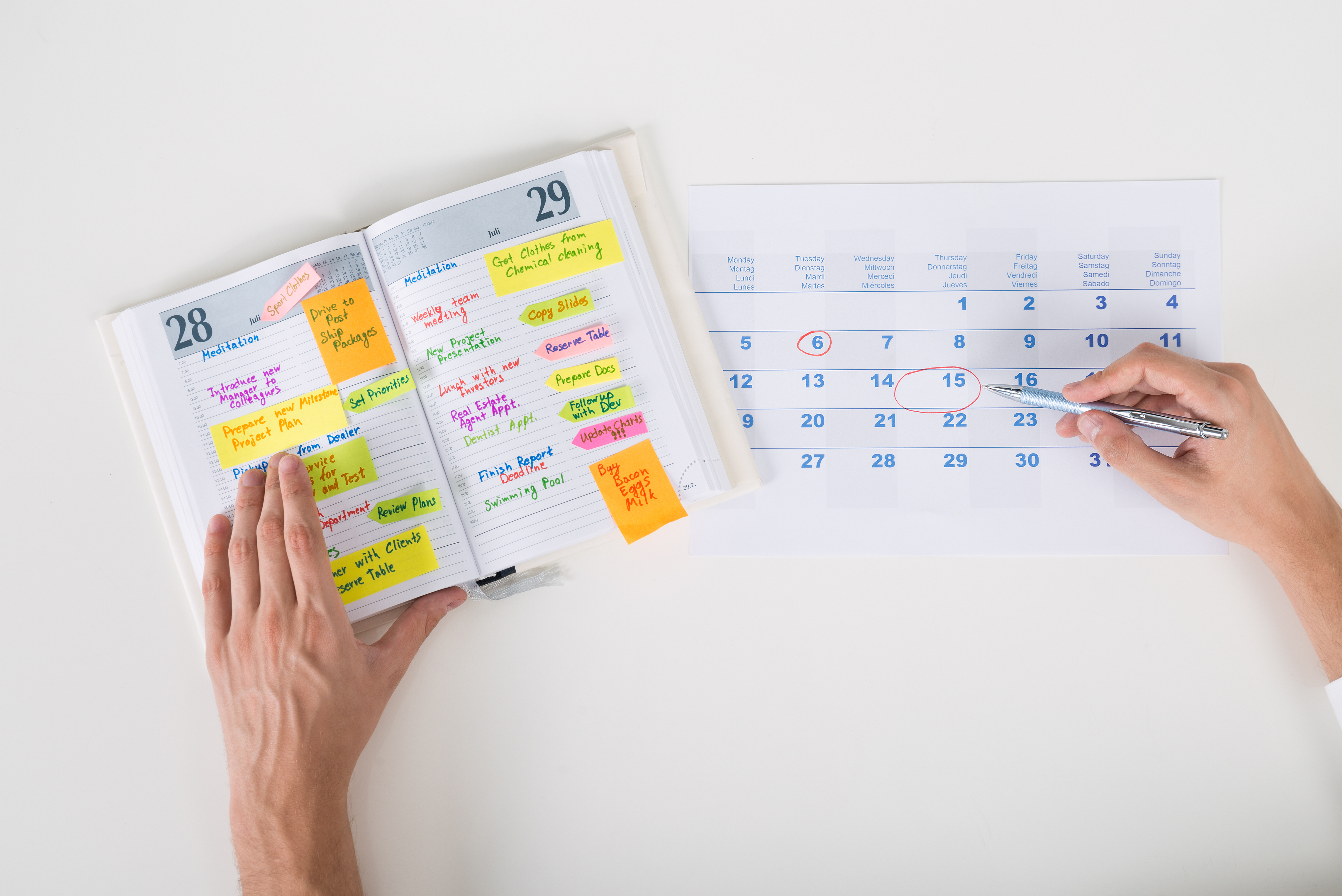 Close-up Of Person Hands Highlighting Date On Calendar With Diary At Desk