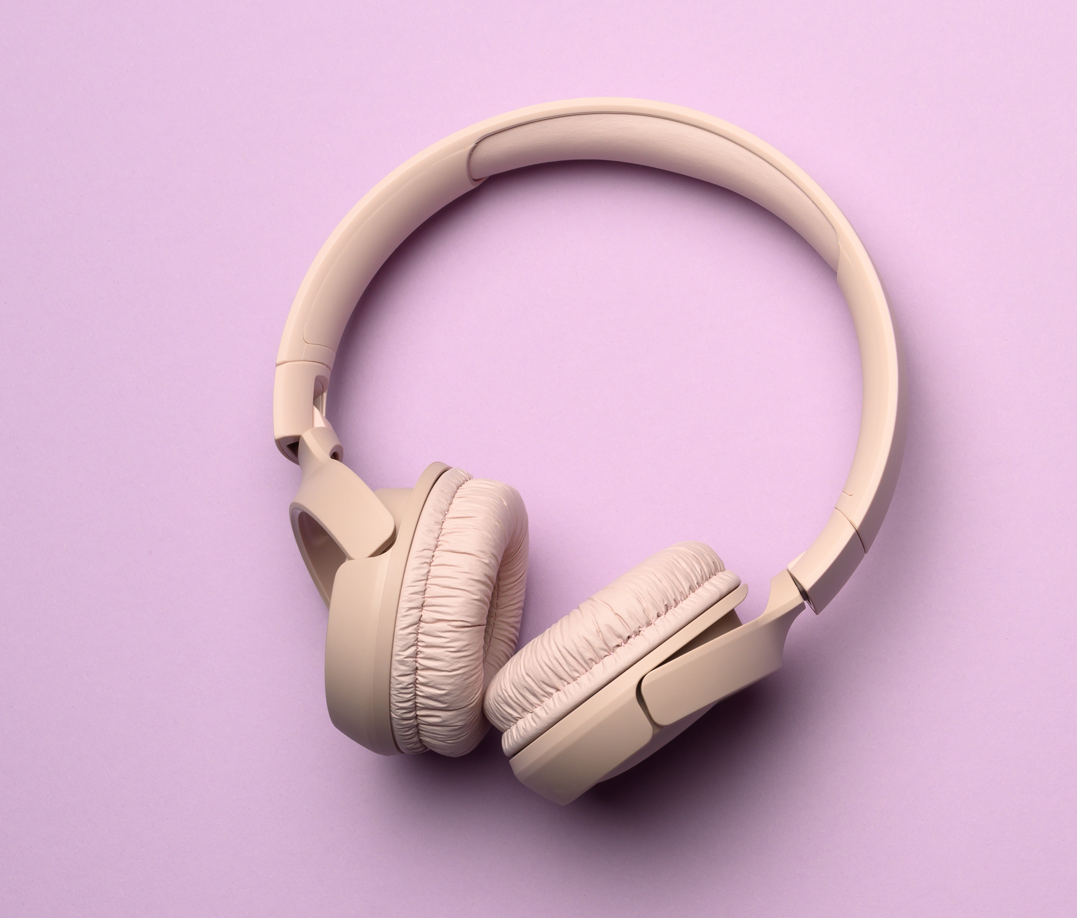 beige wireless headphones on a purple background. Top view on modern gadget