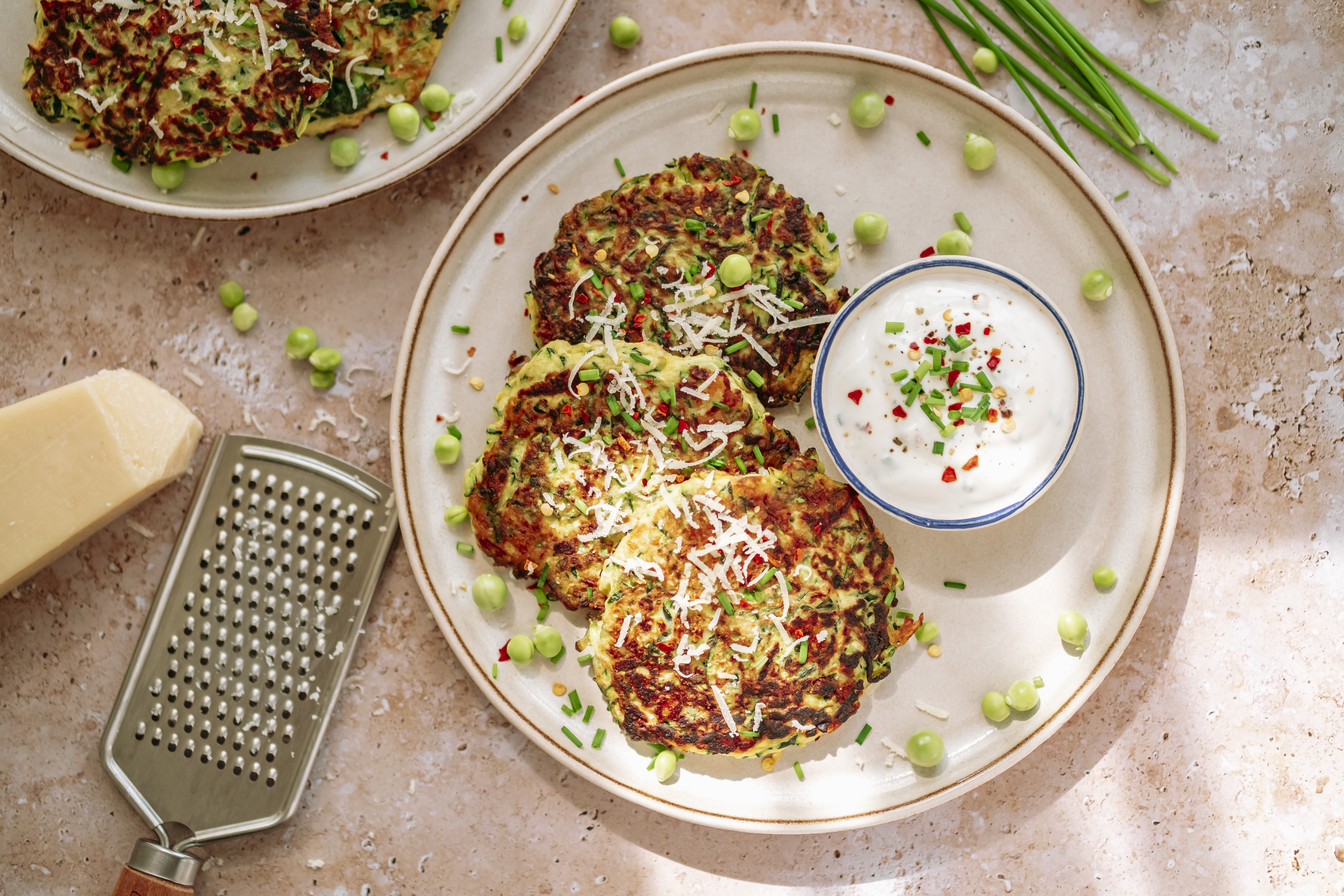 zucchini pancake, peas, chives, grated parmesan,cheese grinder, pot of spicy cream, in white plate