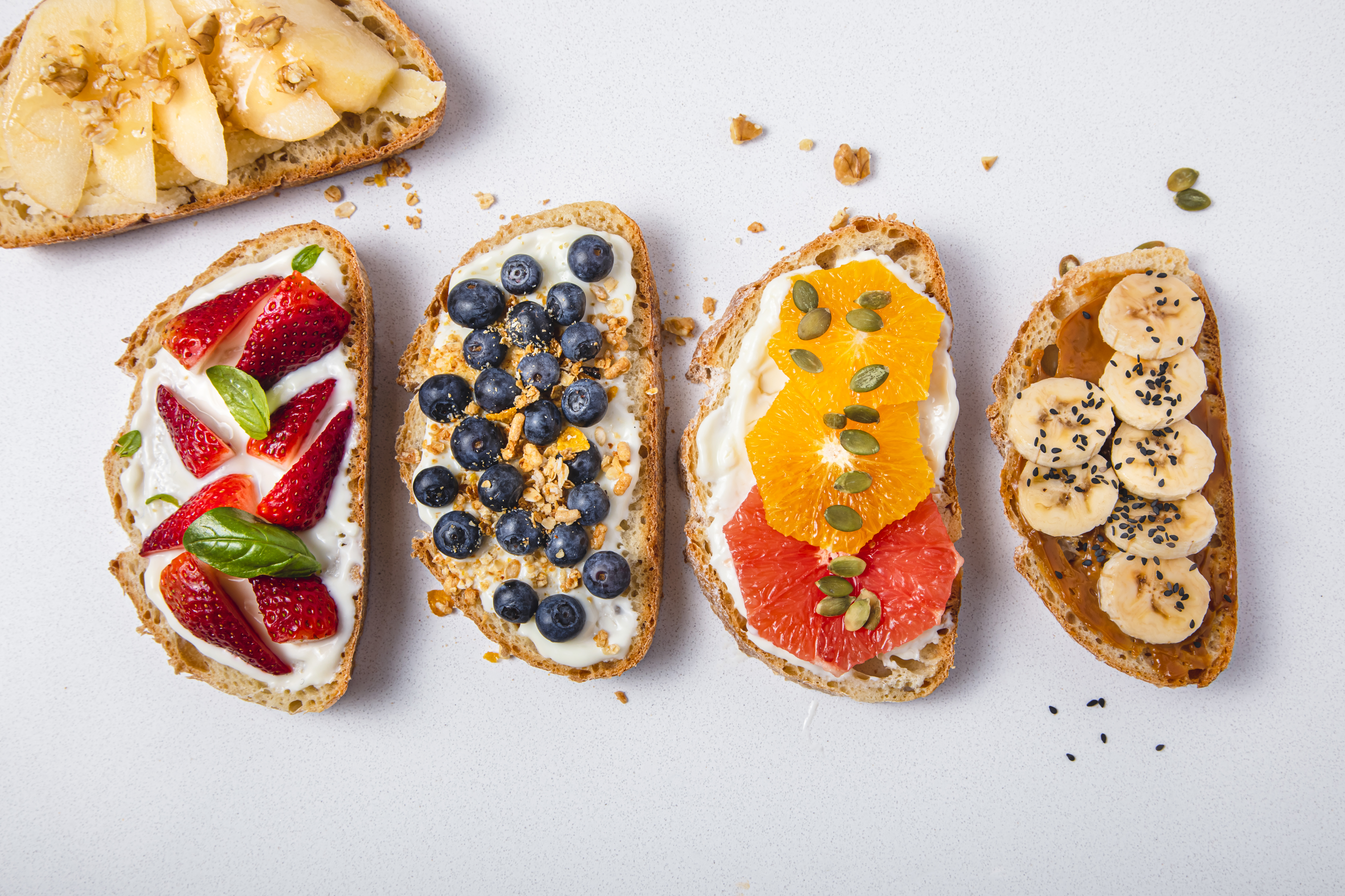 High angle view of toasts with fruits (strawberries, blueberries, banana, apple, orange and grapefruit) for breakfast or snack on white marble background, studio shot.