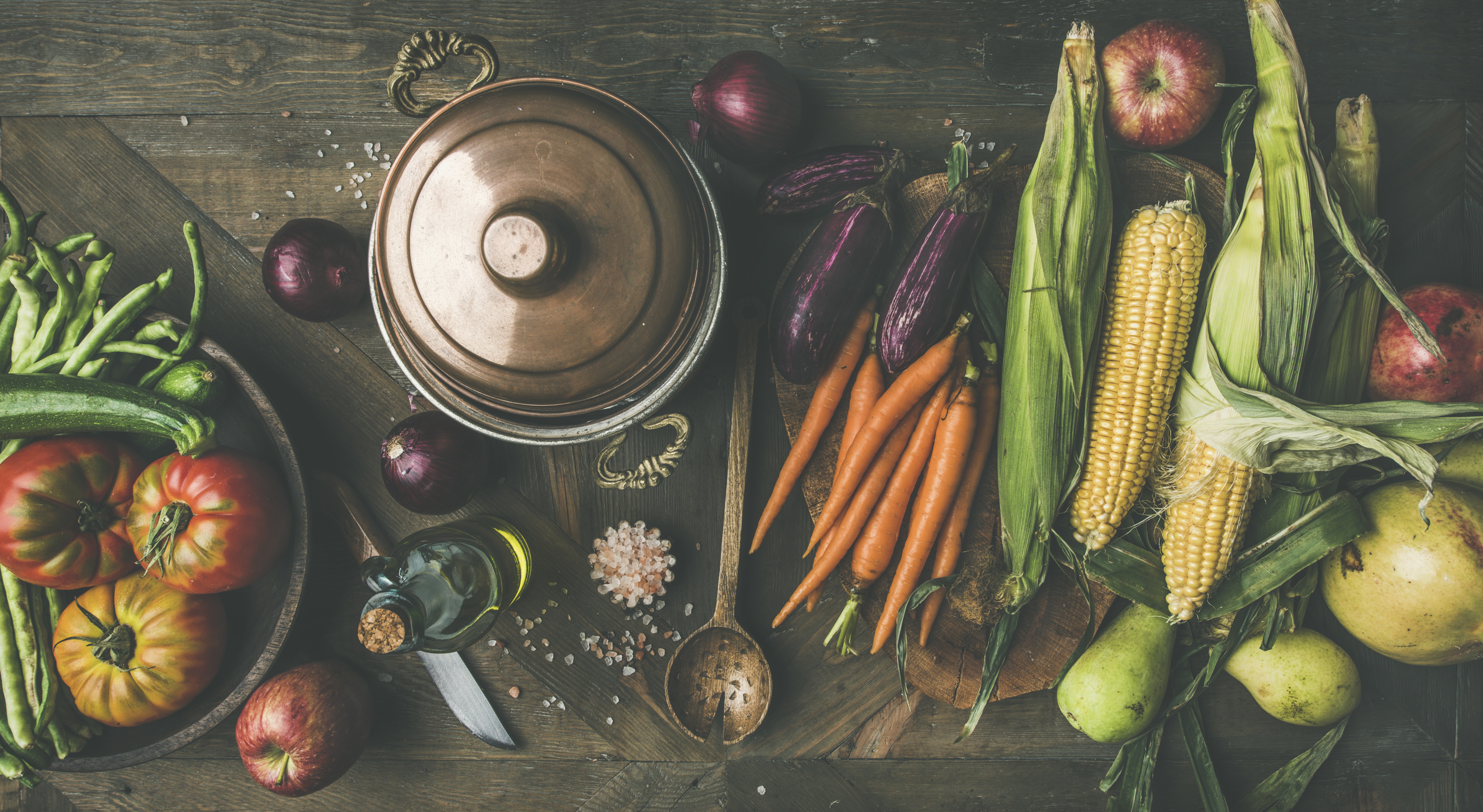 Fall cooking background. Autumn ingredients for Thanksgiving day dinner preparation. Flat-lay of green beans, corn cobs, carrot, tomatoes, eggplant, pears, apples over rustic wooden table, top view