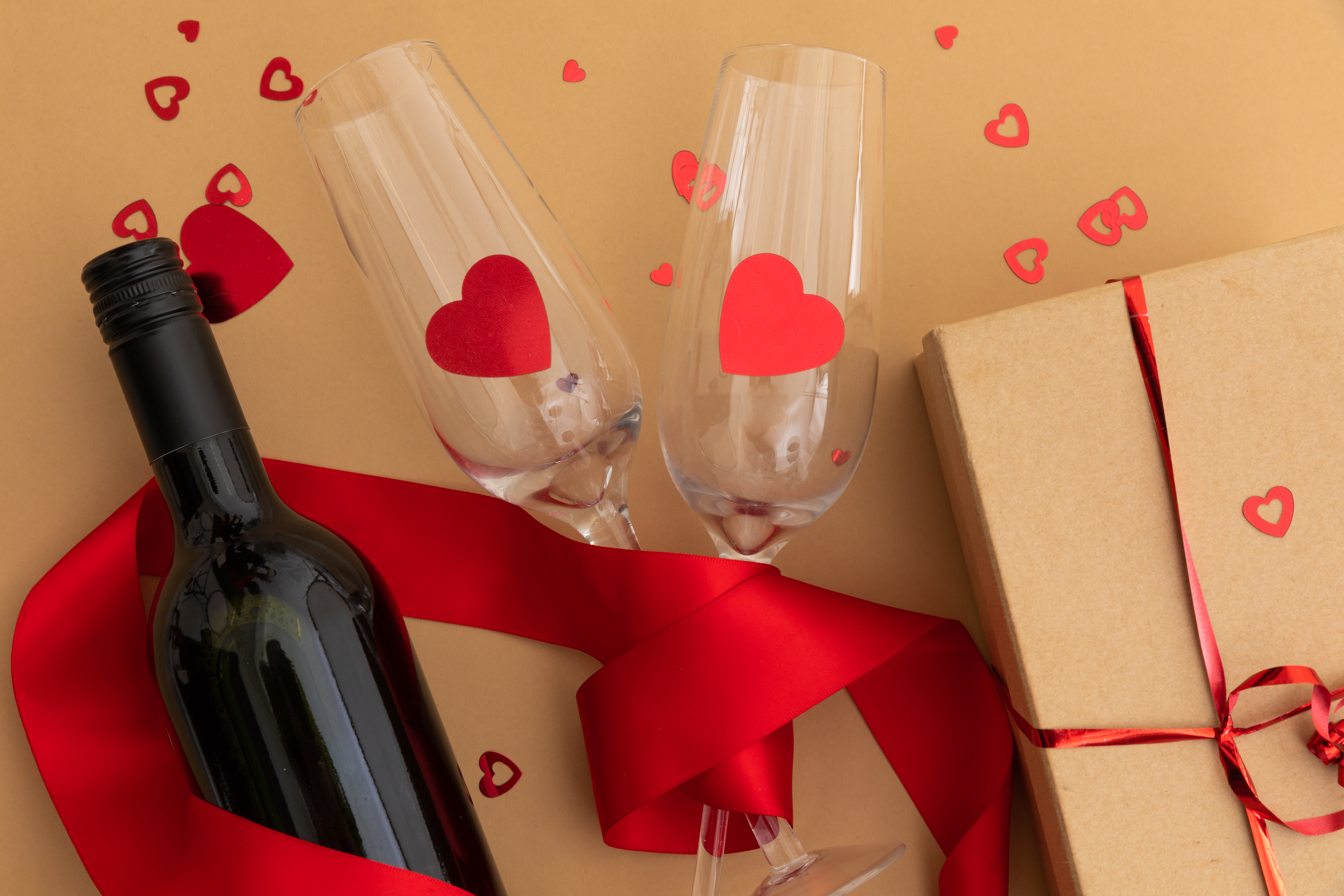 Bottle of wine, glasses with red hearts and present on brown background. valentine's day romance love copy space concept.