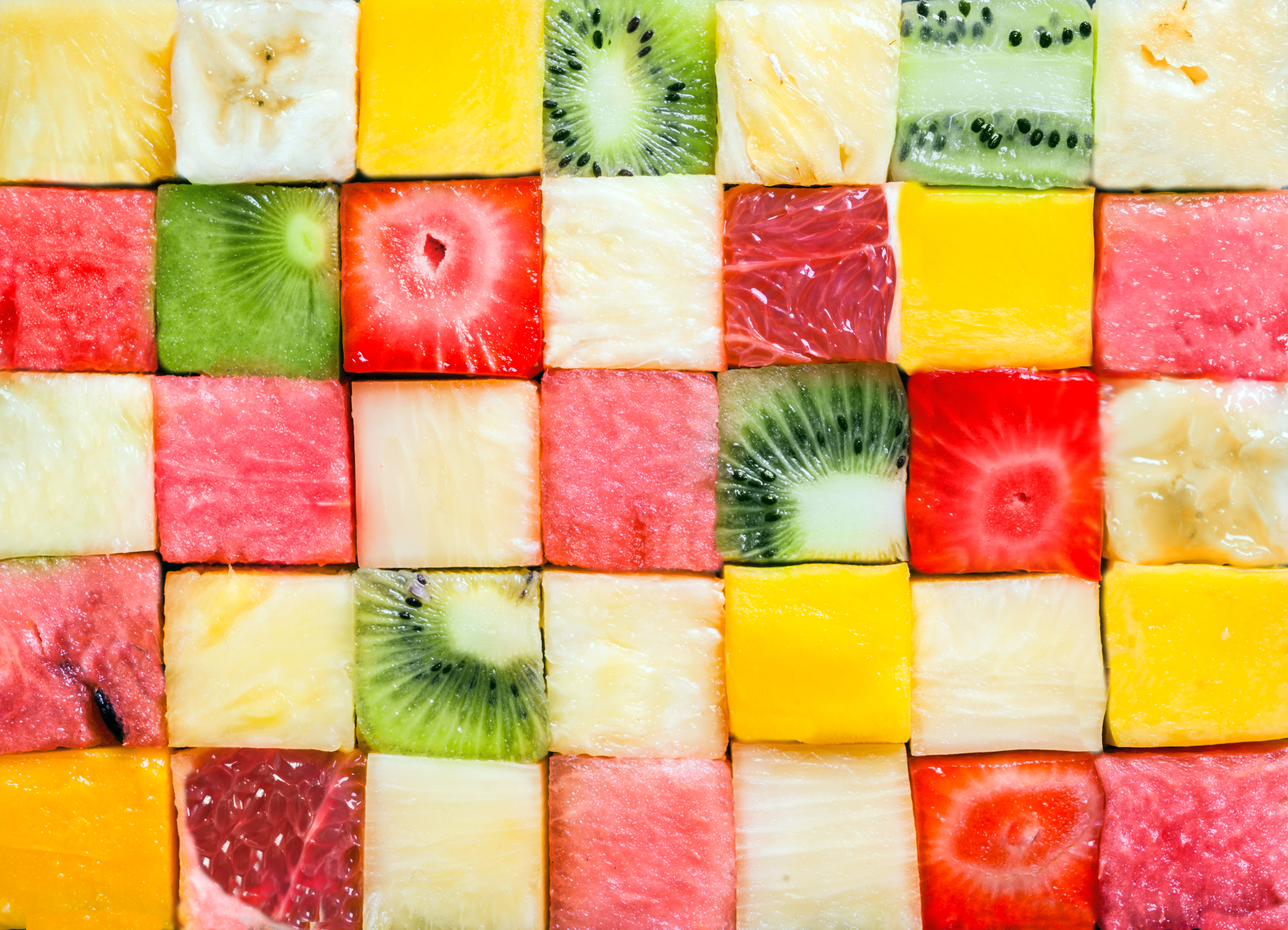 Seamless background pattern and texture of colourful fresh diced tropical fruit cubes arranged in a geometric pattern with melon, watermelon, banana, pineapple, strawberry, kiwifruit and grapefruit