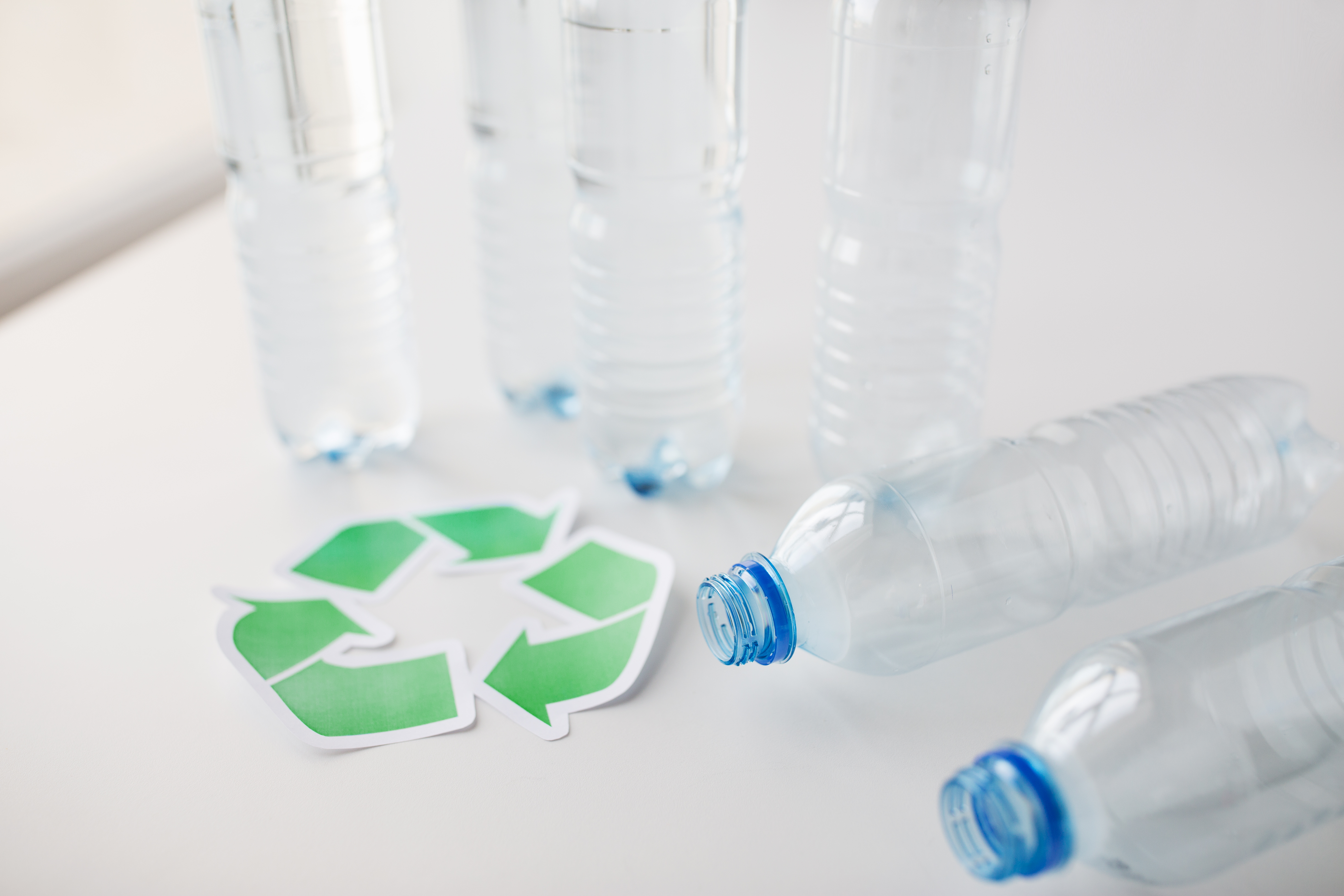 recycling, reuse, garbage disposal, environment and ecology concept - close up of empty plastic water bottles with green recycle symbol on table