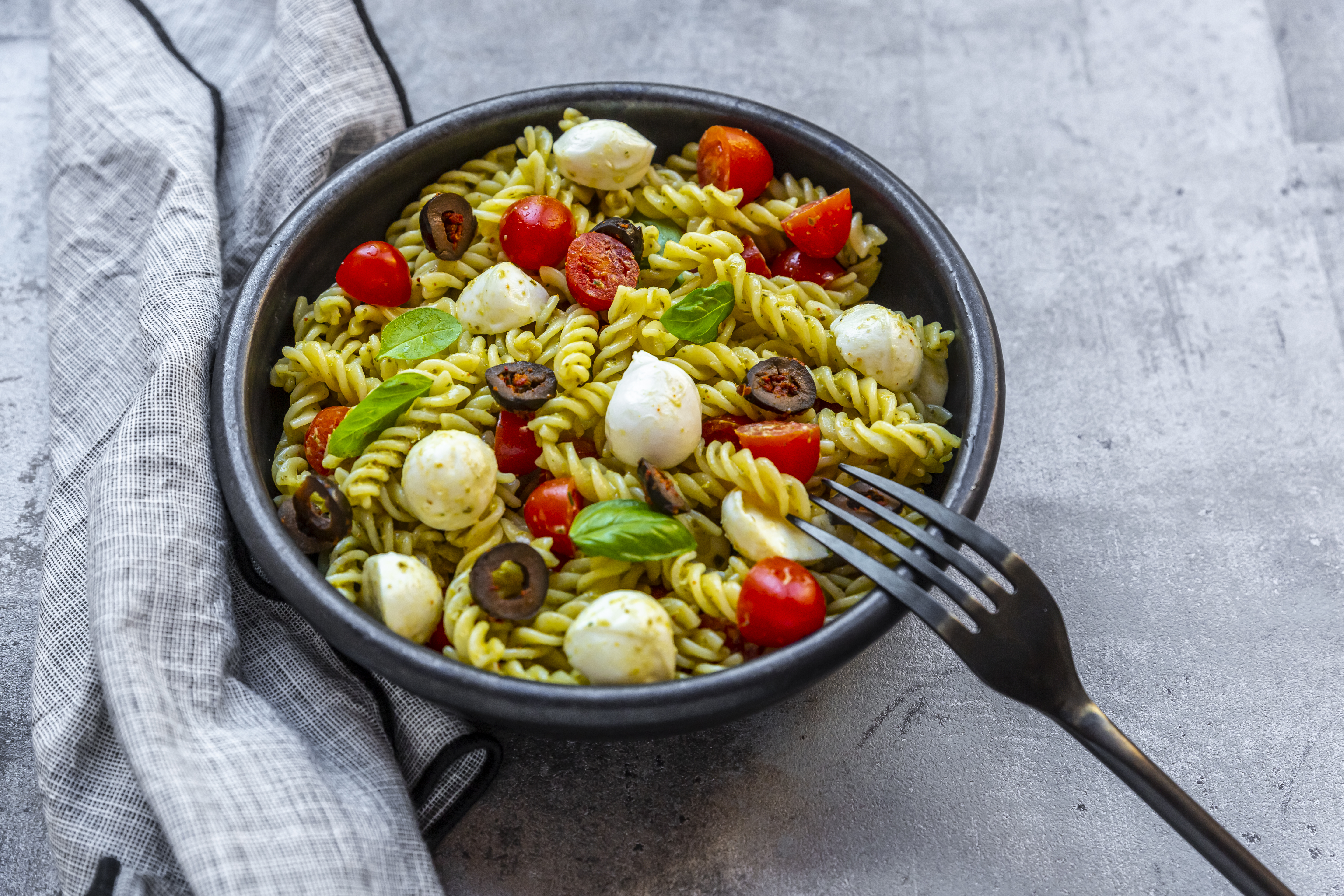 Nudelsalat mit grünem Pesto, Tomaten, Mozzarella, Oliven und Basilikum