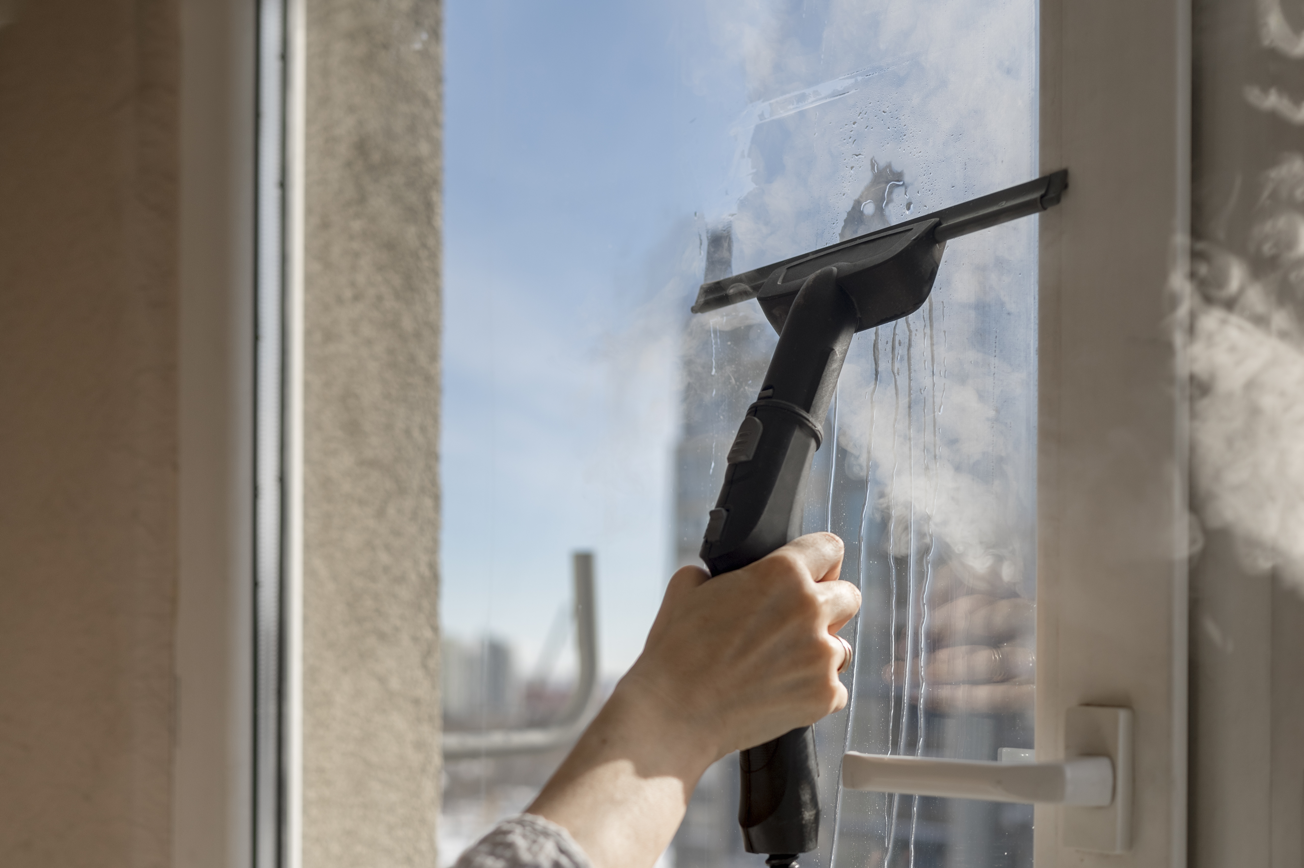 Hand of woman cleaning window with clean steam generator at home