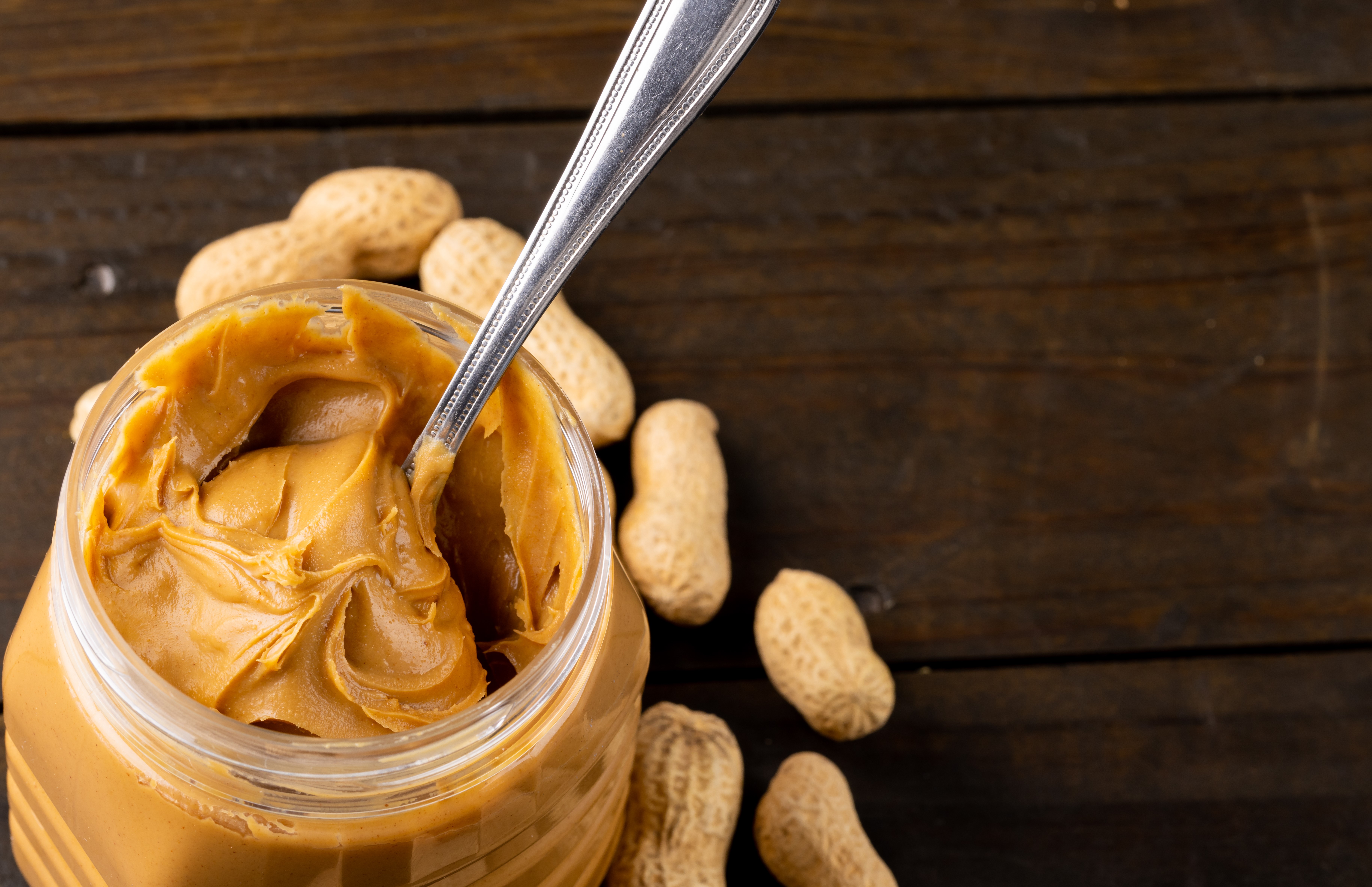 Image of jar with peanut butter and nuts on wooden surface