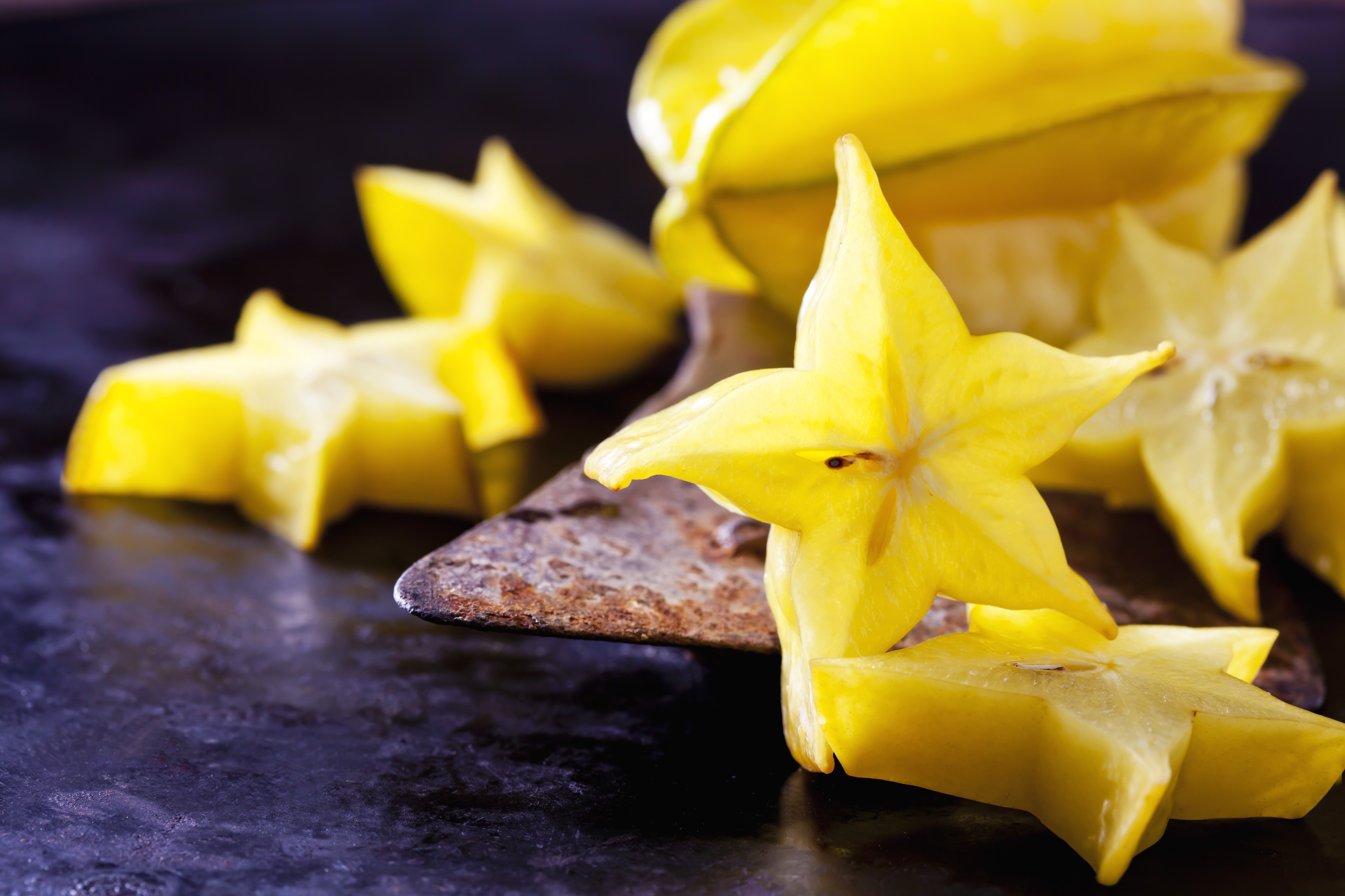 Sternfrucht (Averrhoa carambola), Karambole, Sternfrucht, Scheiben, Obst, Früchte, gelb, altes Hackmesser, dunkler Untergrund