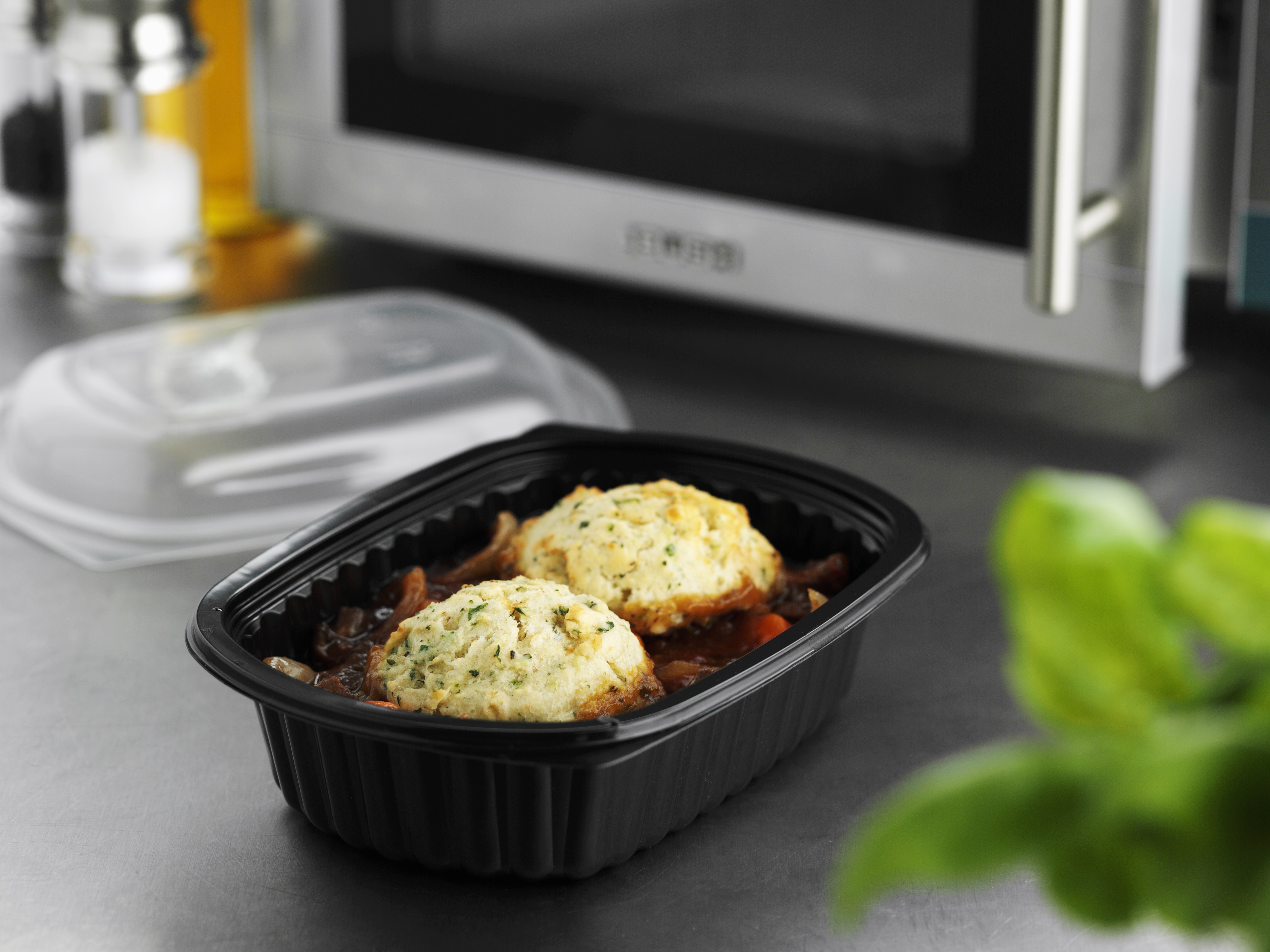 Beef stew in plastic container in front of microwave oven