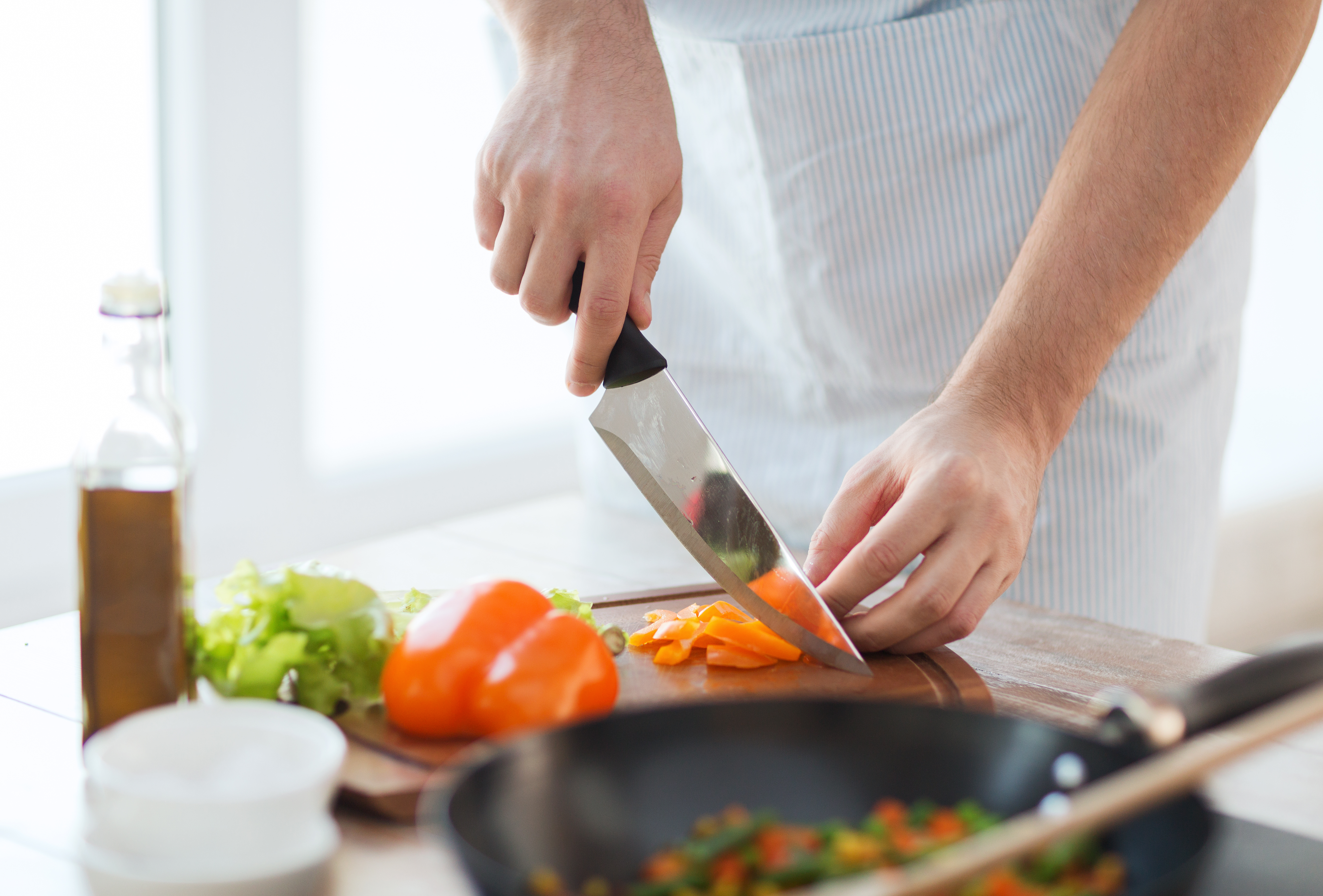 cooking, food and home concept - close up of male hand cutting pepper on cutting board at home