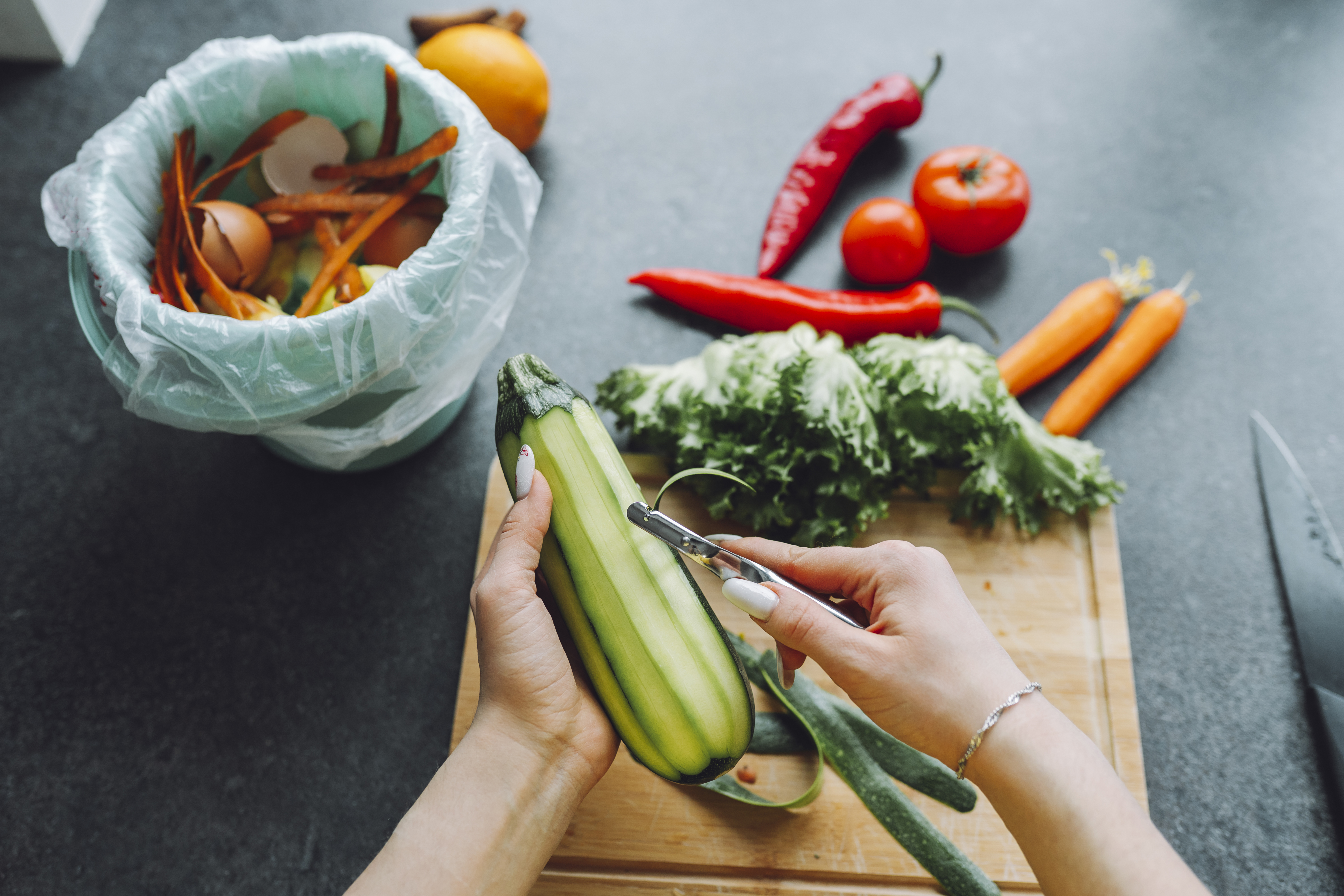 Hands of woman peeling zucchini on kitchen counter at home