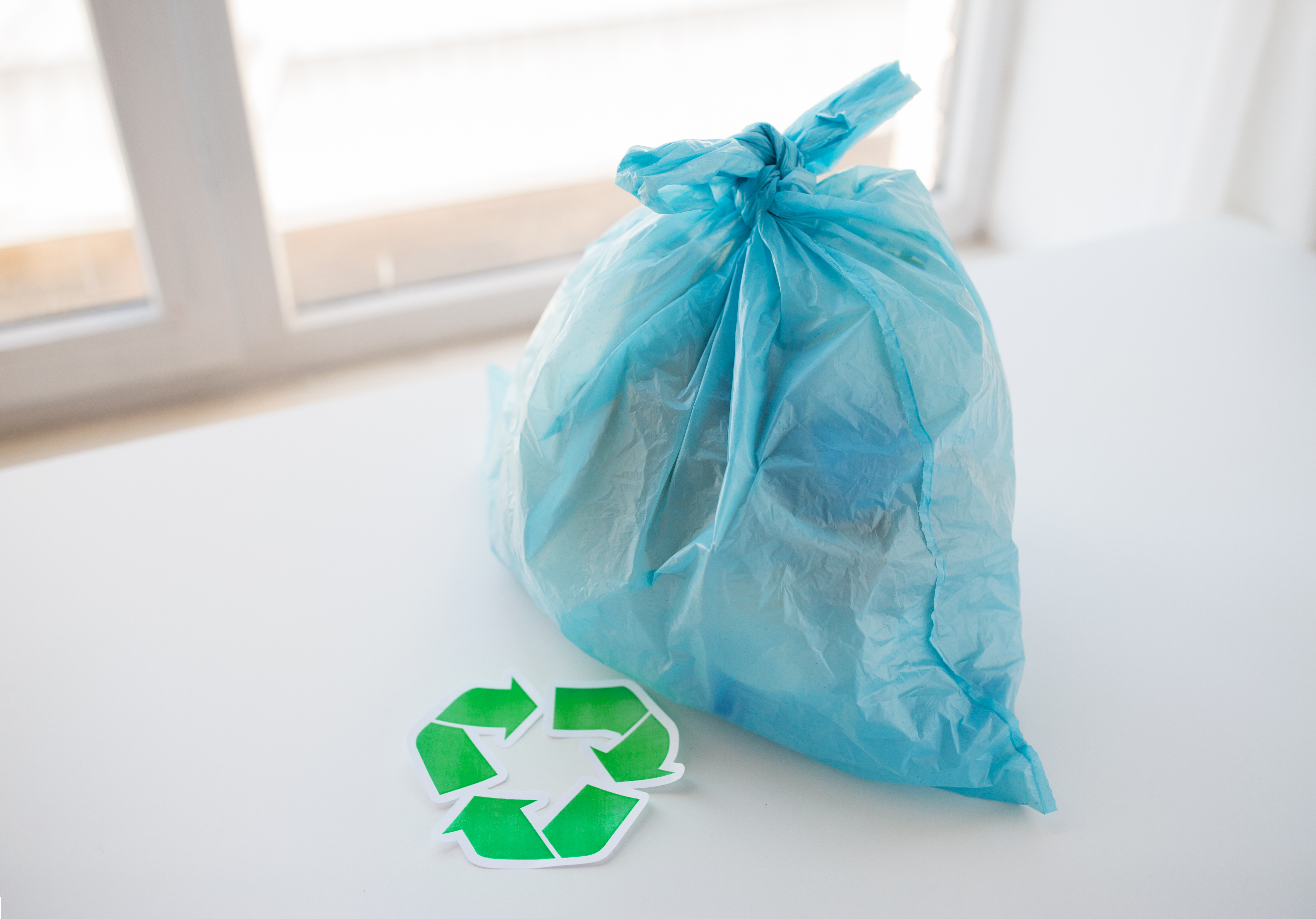waste recycling, reuse, garbage disposal, environment and ecology concept - close up of rubbish bag with trash or garbage and green recycle symbol at home