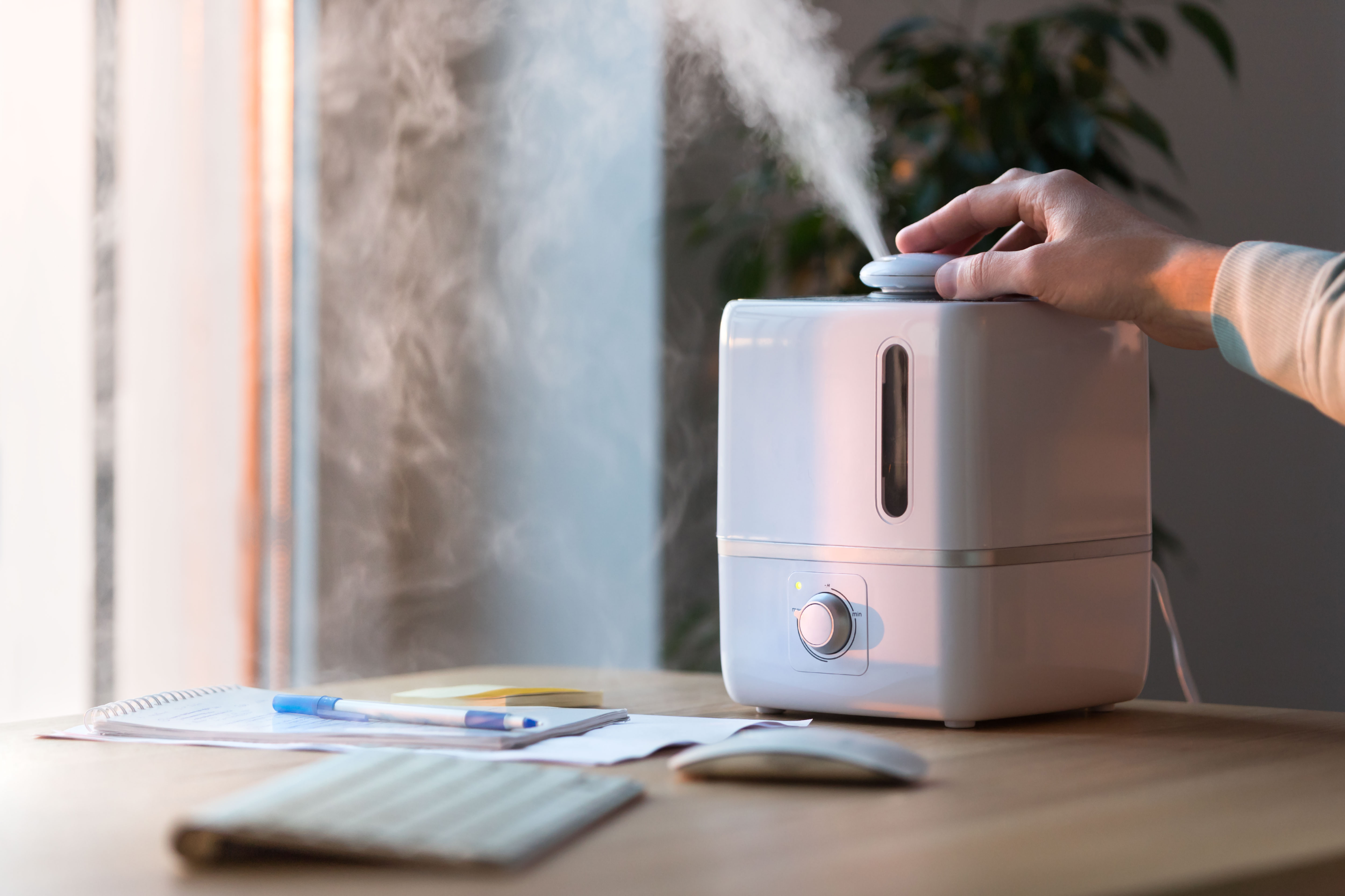Man using aroma oil diffuser on the table, steam from humidifier, selective focus. Humidification of air in the apartment during the period of self-isolation. Remote work, working home.